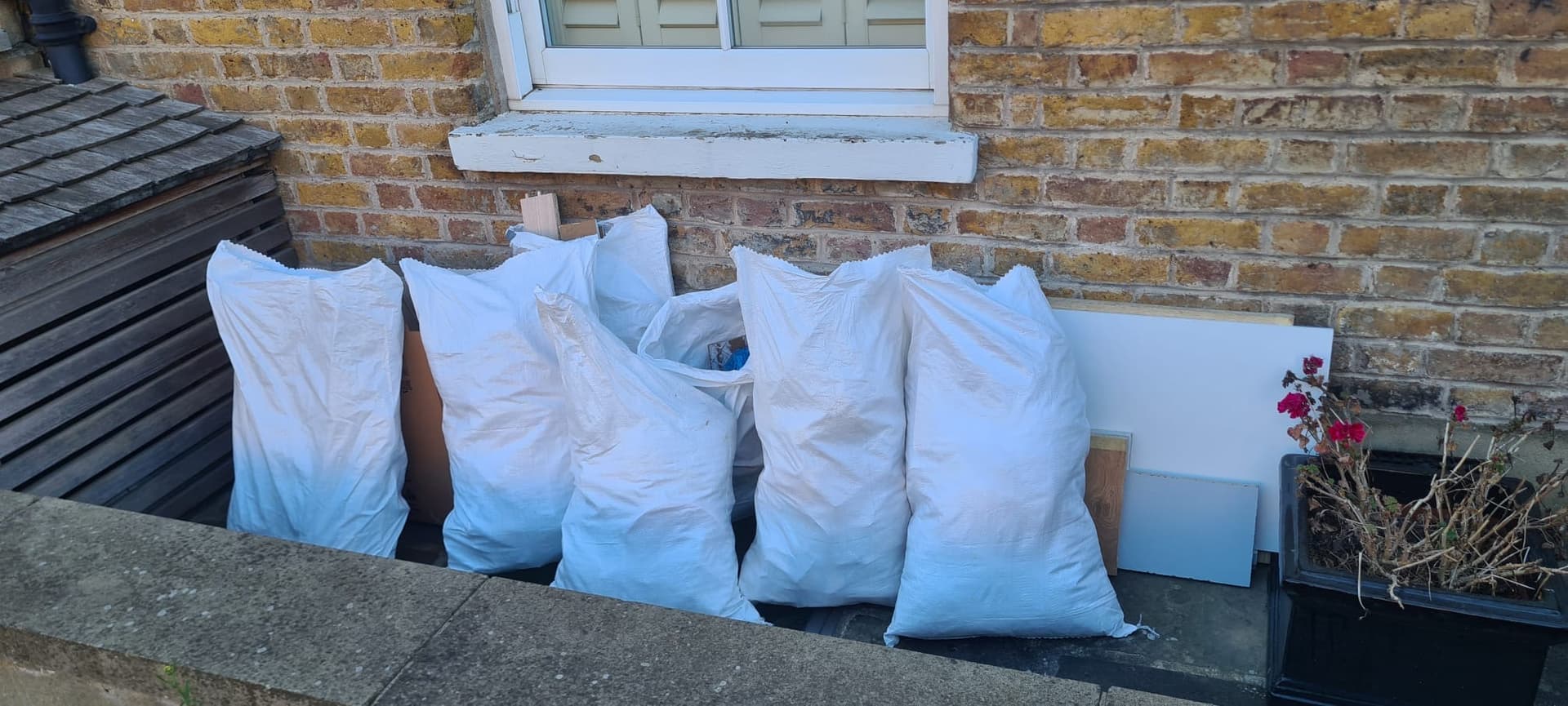 Six white builder rubble sacks lined up against a yellow brick wall in Meopham, ready for Andy's pickup