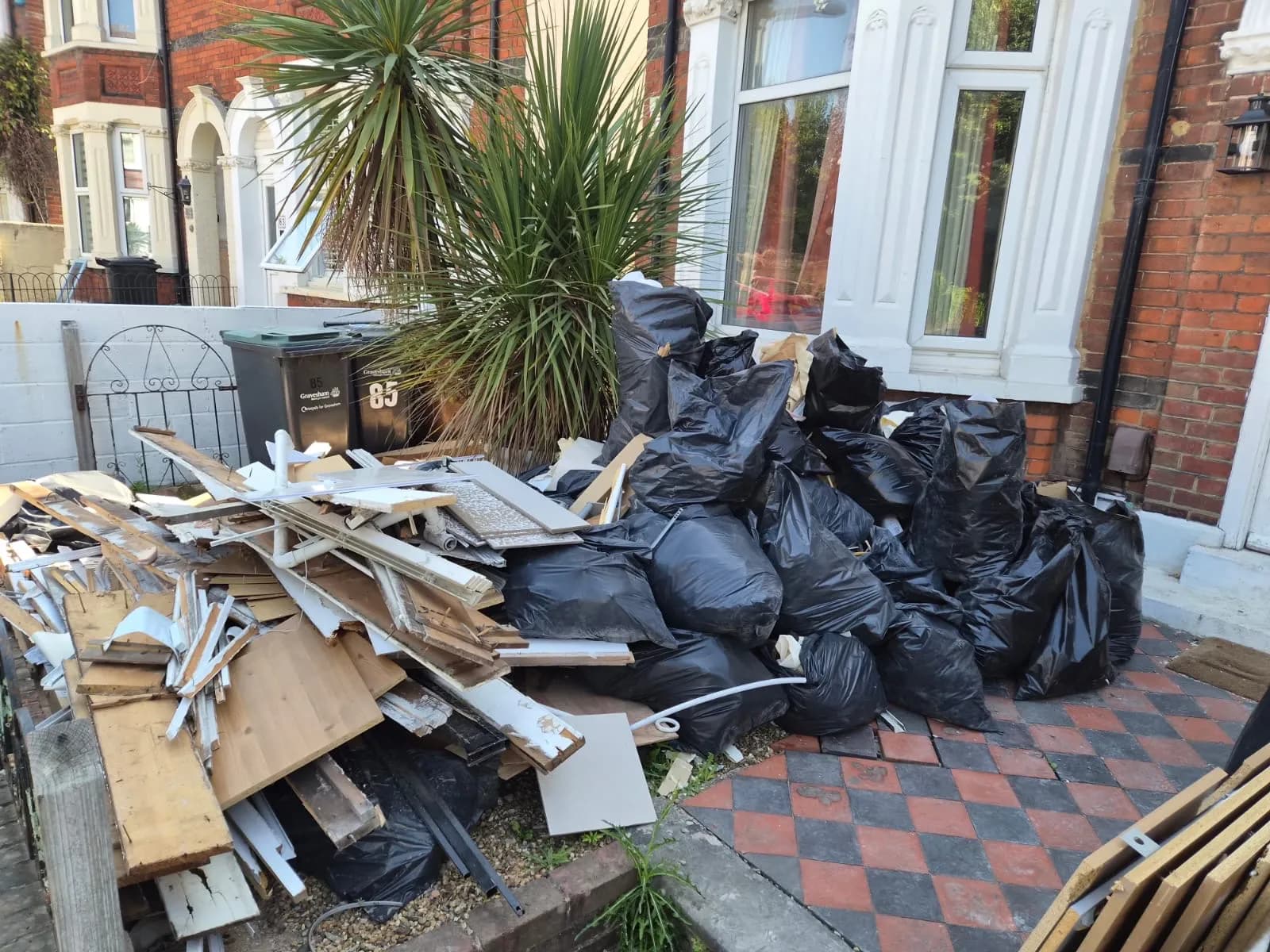 The front garden of a terraced house in Gravesend piled with black rubbish bags and old wood from a refurbishment before Andy cleared it