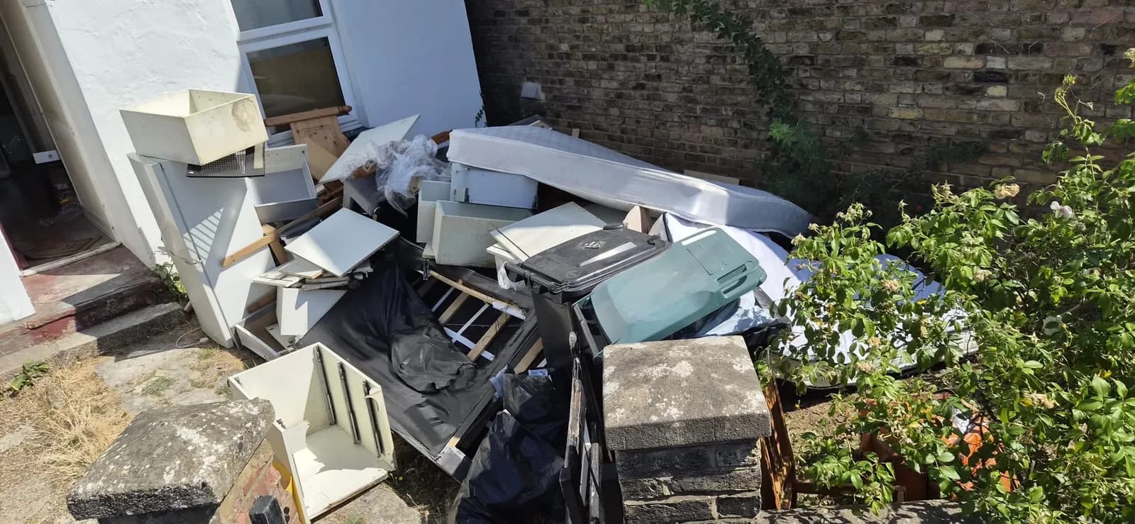 A full house clearance piled outside a white house in Gravesend — mattress, bed base, wardrobe and drawers waiting for Andy to load