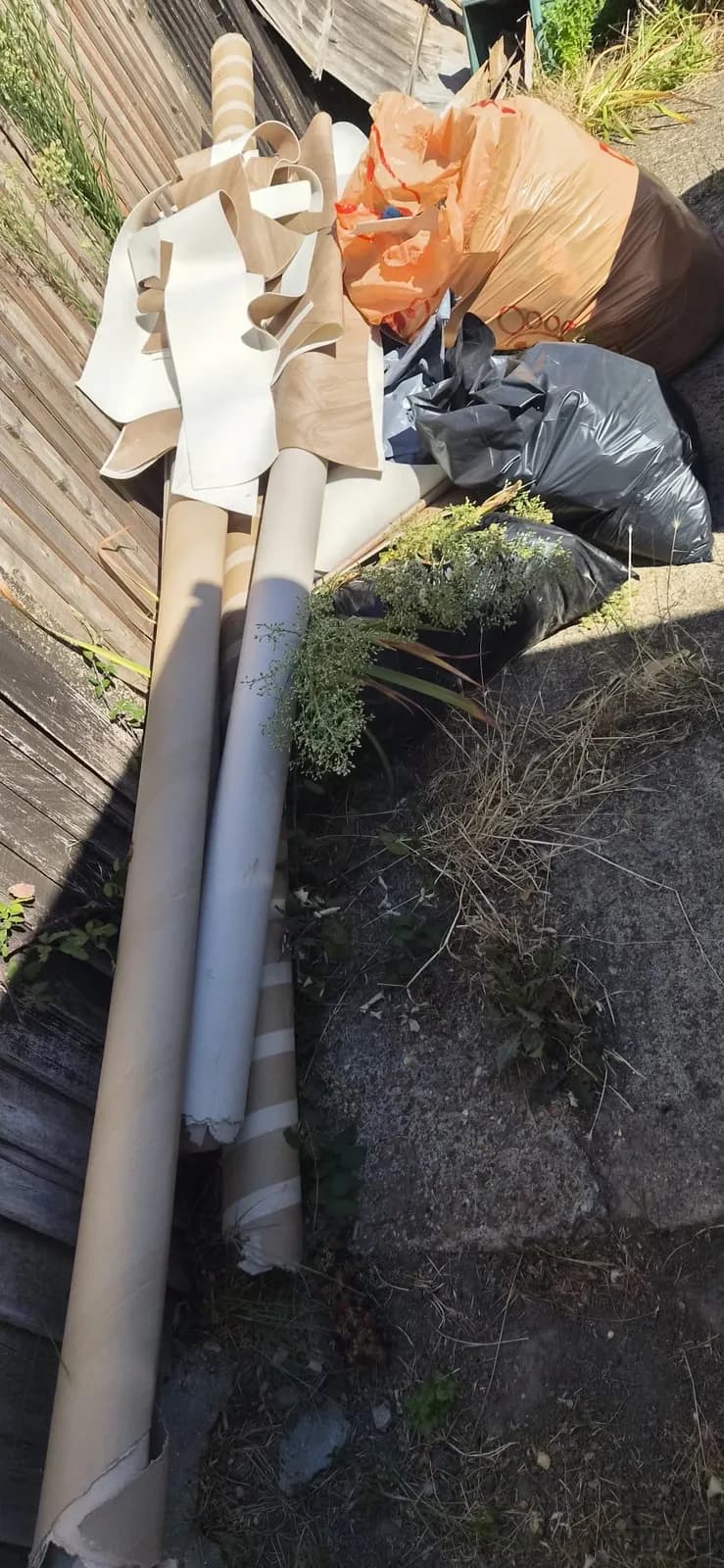 Cardboard tubes, lino offcuts and rubbish bags from an old flooring job piled by a fence in Northfleet