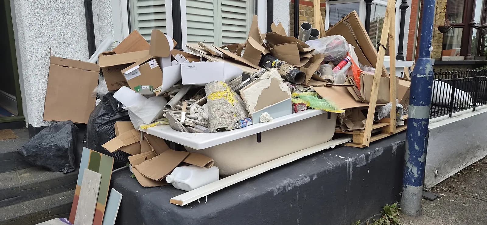 An old bath full of plaster, cardboard and pipe offcuts on the front step of a house in Gravesend, with more renovation waste stacked around it
