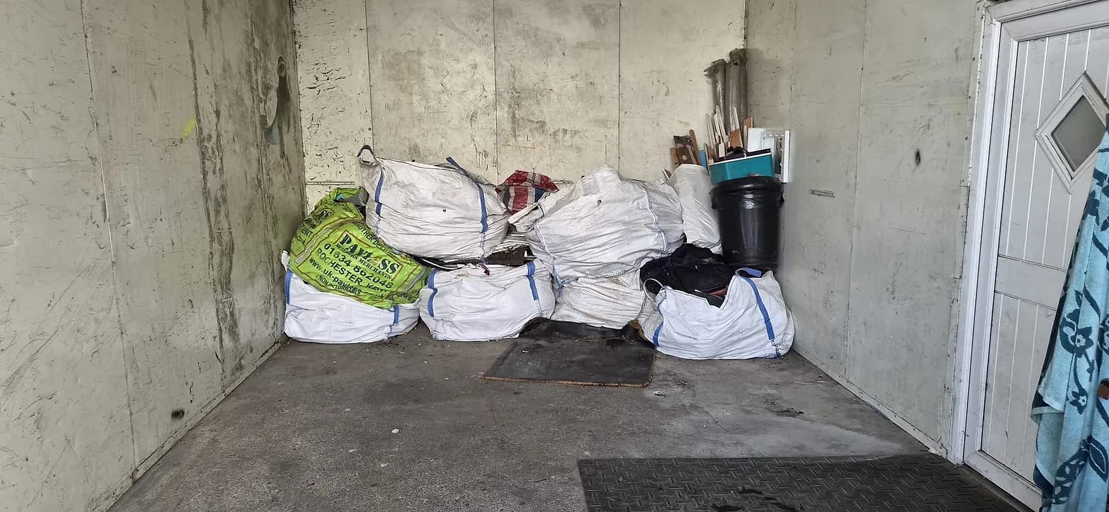 Six white bulk bags of rubble and a stack of old timber inside a garage in Gravesend before clearance