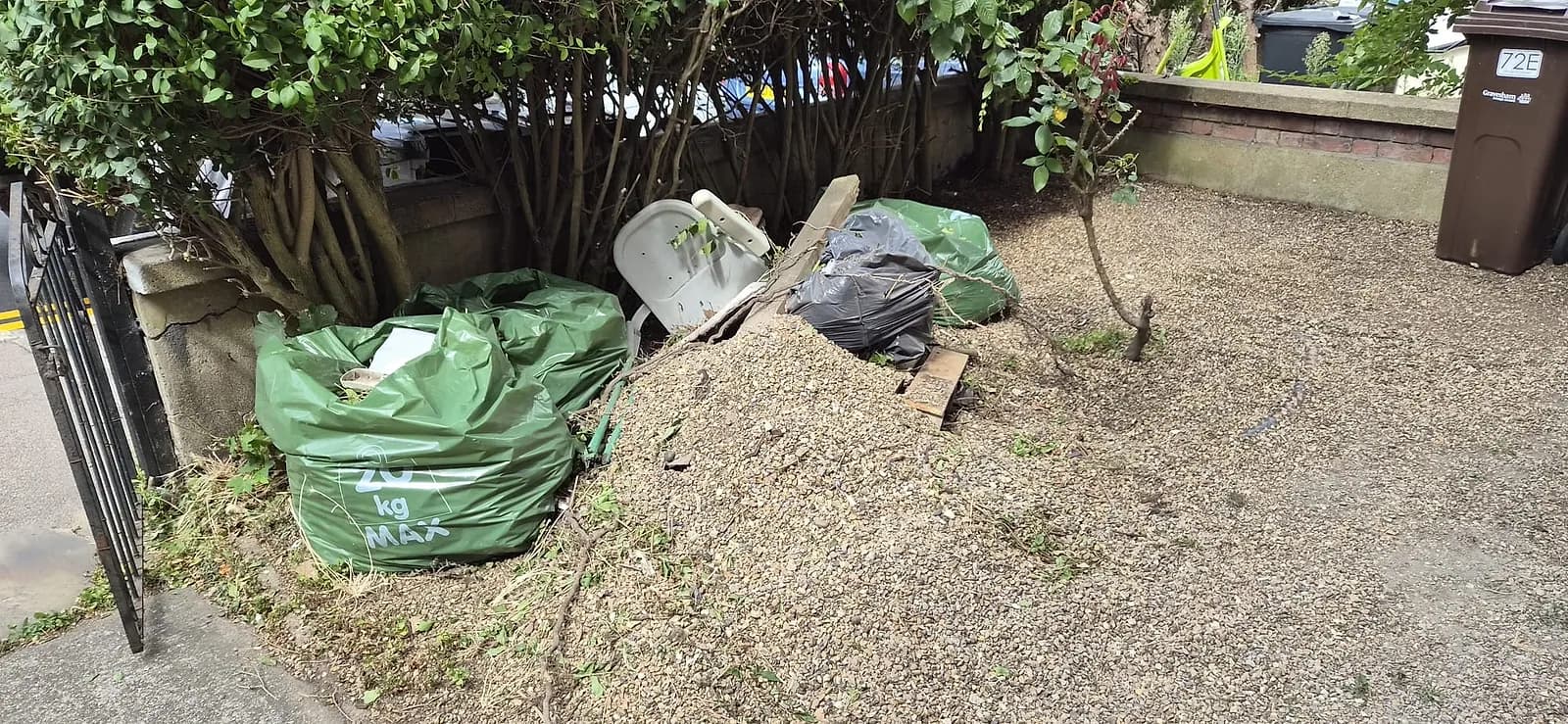 Green garden waste sacks, a black bag, a plastic chair and a small gravel heap waiting by a front gate in Gravesend