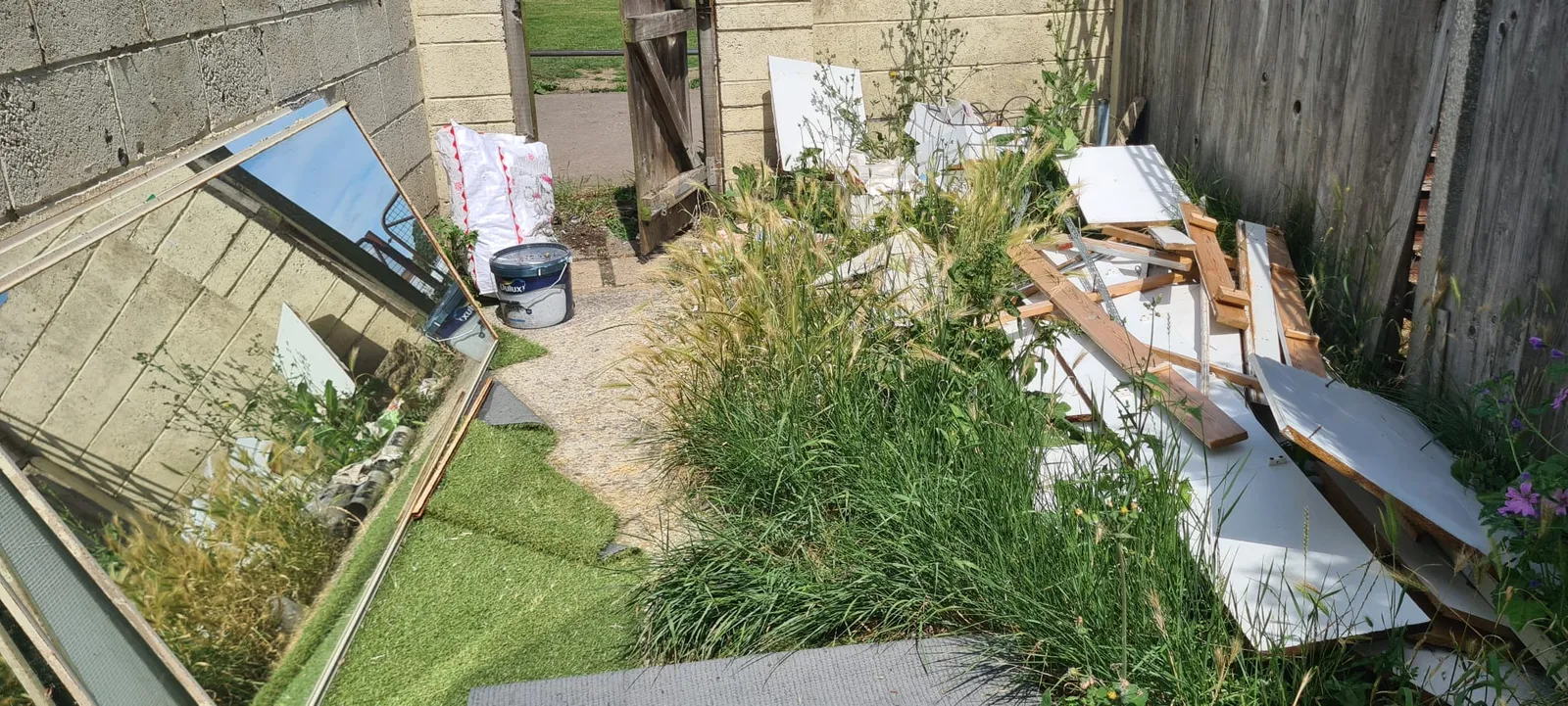 A garden in Northfleet with an old mirror, boards, timber and a tub of paint piled in the corner before Andy cleared it