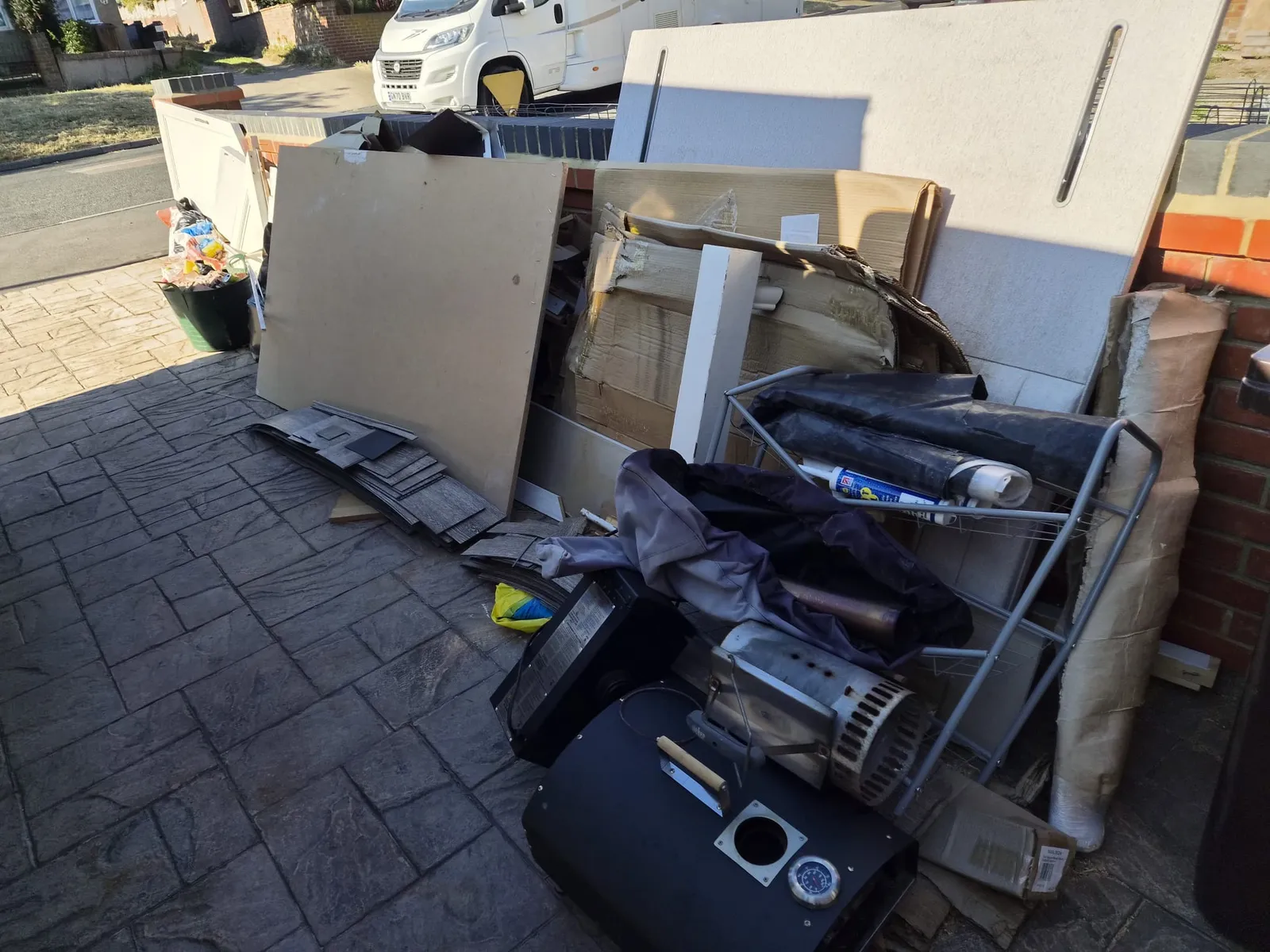 A block-paved driveway in Gravesend covered with old boards, a broken barbecue, a clothes airer and bags of household waste before clearance