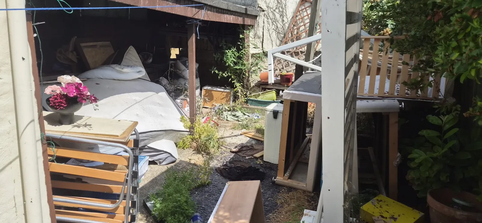 A mattress, garden chairs and old furniture filling a lean-to and back garden in Gravesend before clearance