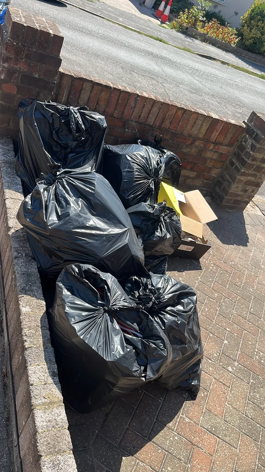 Black rubbish bags and cardboard boxes stacked inside a front garden wall in Gravesend before collection