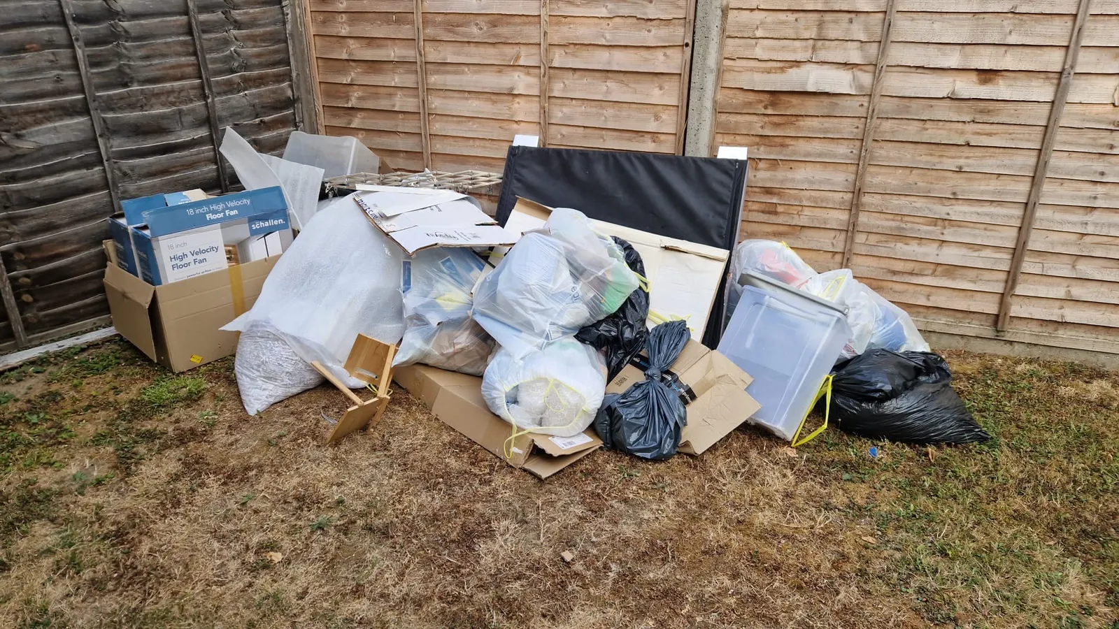 Cardboard boxes, bubble wrap and rubbish bags piled on a dry back lawn against a fence in Gravesend