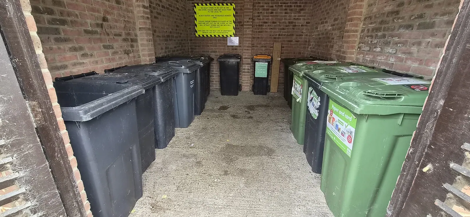 The same Gravesend bin store after clearance — black bins and green recycling bins lined up either side, floor swept clean