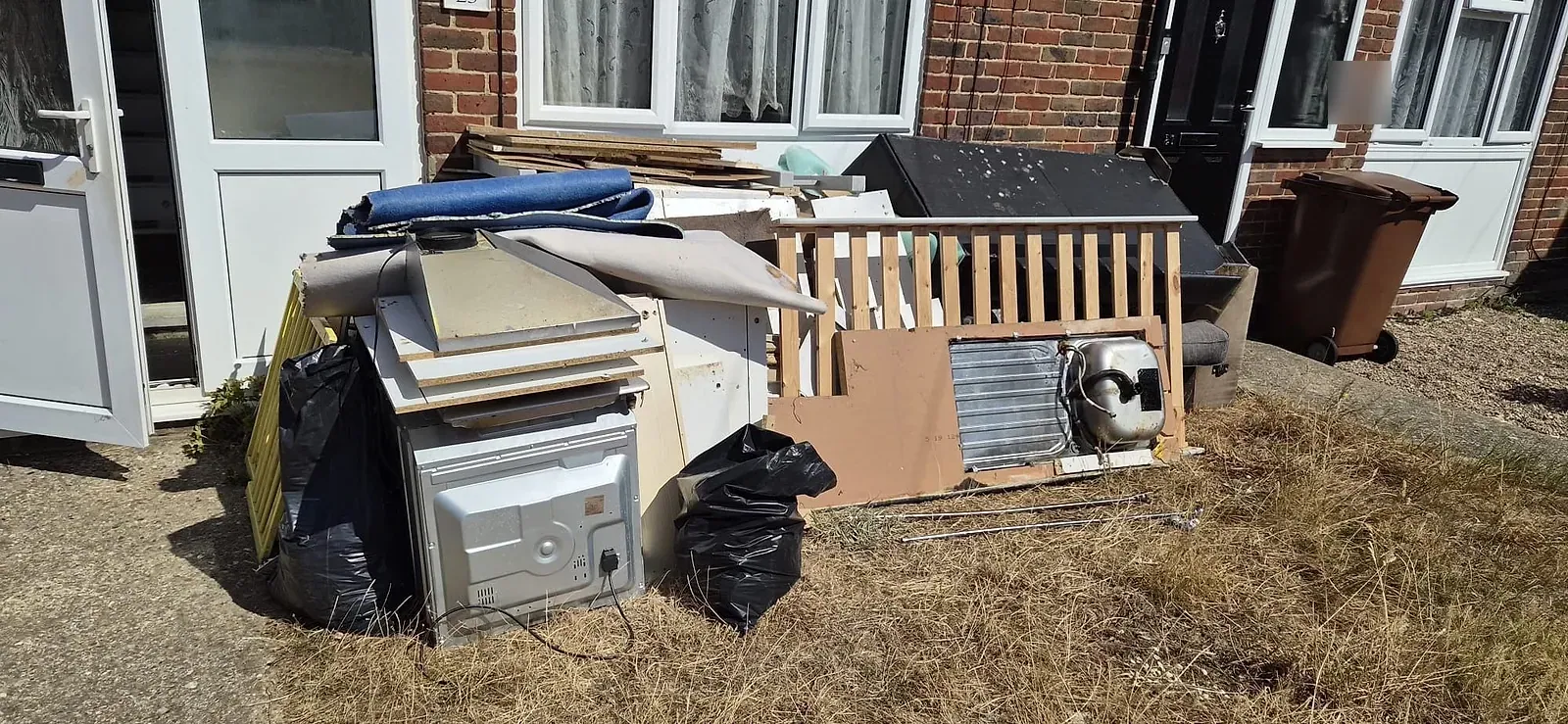 Old kitchen units, a built-in oven, rolls of carpet, a sink in worktop and stair spindles piled on a front lawn in Gravesend