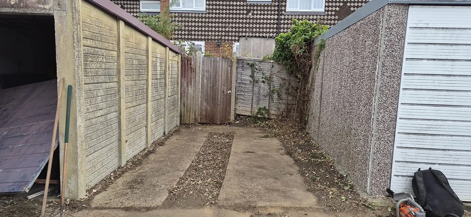 The alley between the same two Gravesend garages cleared back to concrete, fence and gate visible again