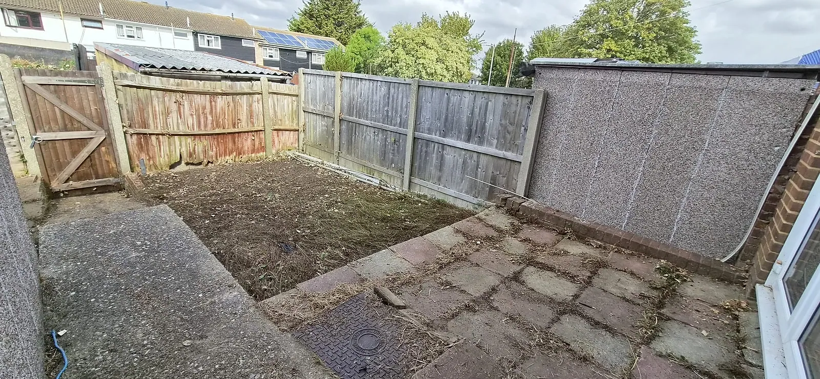 The same Gravesend back garden cleared to bare soil with the patio slabs swept and the fences and gate visible
